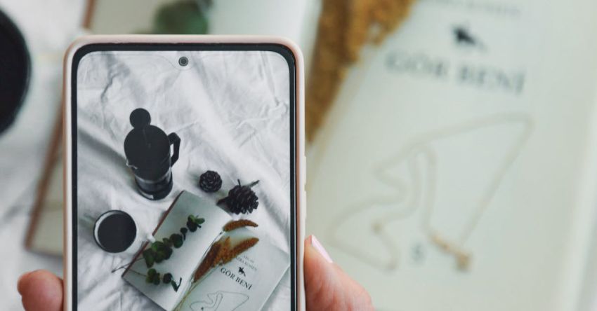 Aesthetic Packaging - A person holding a smartphone with a photo of a book and a candle